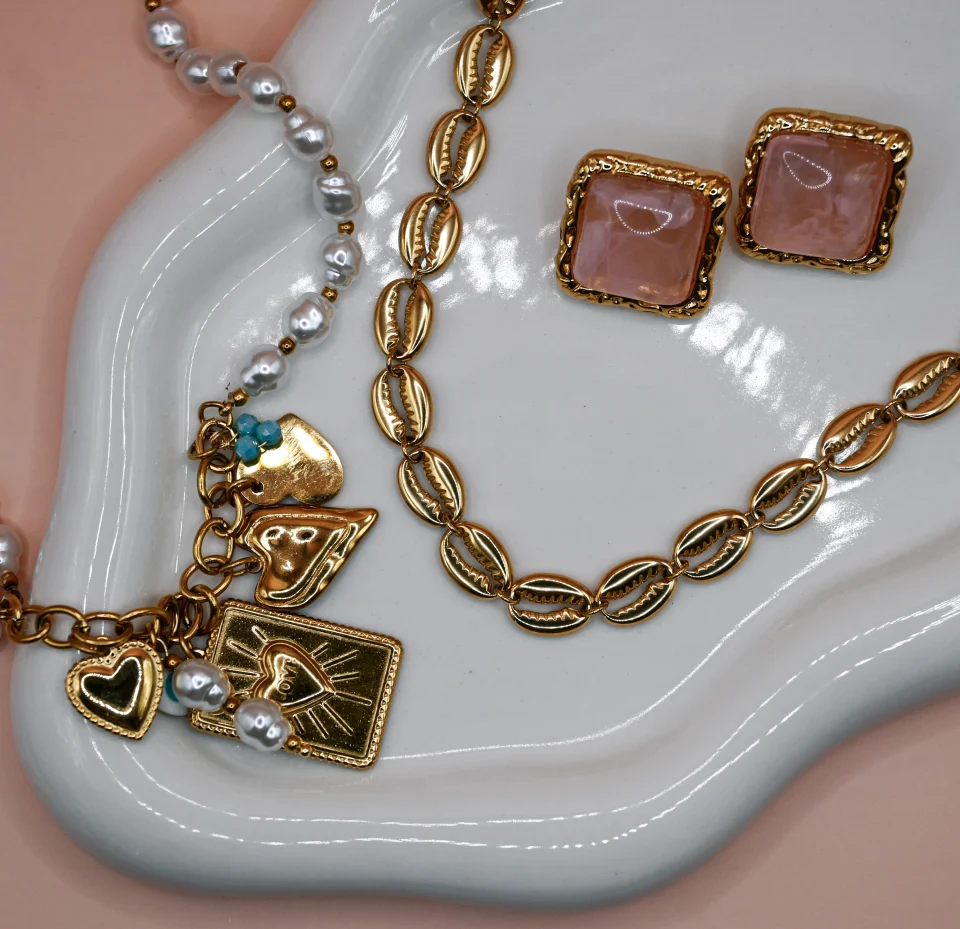 Love Pearl Charm Necklace with gold-plated steel chain featuring elegant pearls and hanging charms including steel hearts in various designs, multiple pearls, peephole, and turquoise beads. Adorned with a central identity ‘Love’ charm.