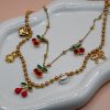 Gold steel charm necklace with cherries, teddy bear, pearl, heart, and bow steel charms on a trendy steel bead chain. Bold spring jewelry for 2026. Hot summer jewelry trends for 2026.