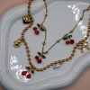 Gold steel charm necklace with cherries, teddy bear, pearl, heart, and bow steel charms on a trendy steel bead chain. Bold spring jewelry for 2026. Hot summer jewelry trends for 2026.