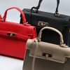Mini red top-handle bag, made of synthetic leather in Italy. Inspired by Hermès’ Mini Kelly Bags, it features the signature metal clasp. It comes with a detachable and adjustable strap in a shade of red.