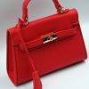 Mini red top-handle bag, made of synthetic leather in Italy. Inspired by Hermès’ Mini Kelly Bags, it features the signature metal clasp. It comes with a detachable and adjustable strap in a shade of red.