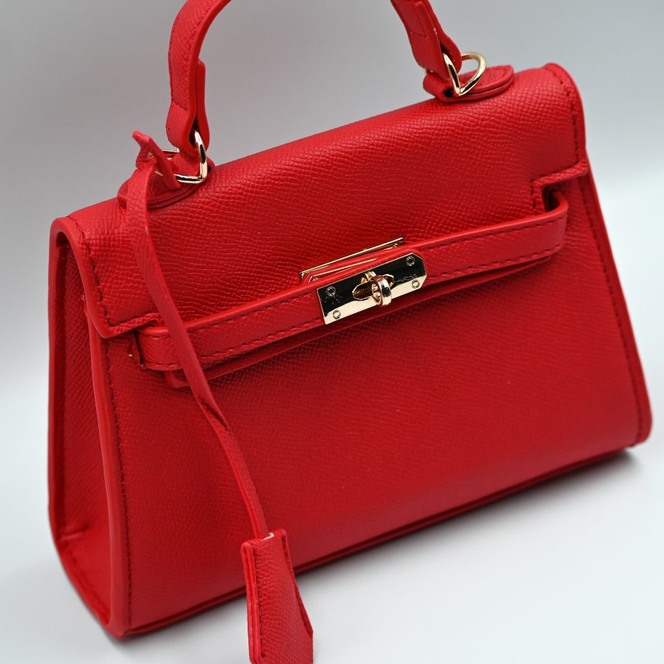 Mini red top-handle bag, made of synthetic leather in Italy. Inspired by Hermès’ Mini Kelly Bags, it features the signature metal clasp. It comes with a detachable and adjustable strap in a shade of red.