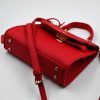 Mini red top-handle bag, made of synthetic leather in Italy. Inspired by Hermès’ Mini Kelly Bags, it features the signature metal clasp. It comes with a detachable and adjustable strap in a shade of red.