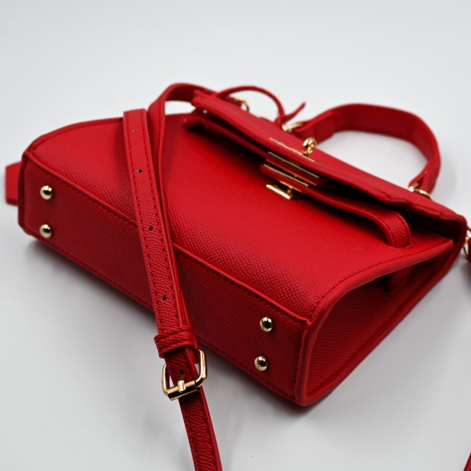 Mini red top-handle bag, made of synthetic leather in Italy. Inspired by Hermès’ Mini Kelly Bags, it features the signature metal clasp. It comes with a detachable and adjustable strap in a shade of red.