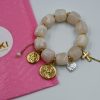 White resin charm bracelet with gold-plated steel details, coins, pearls, chains, and cross charm. A bold and unique summer statement piece.