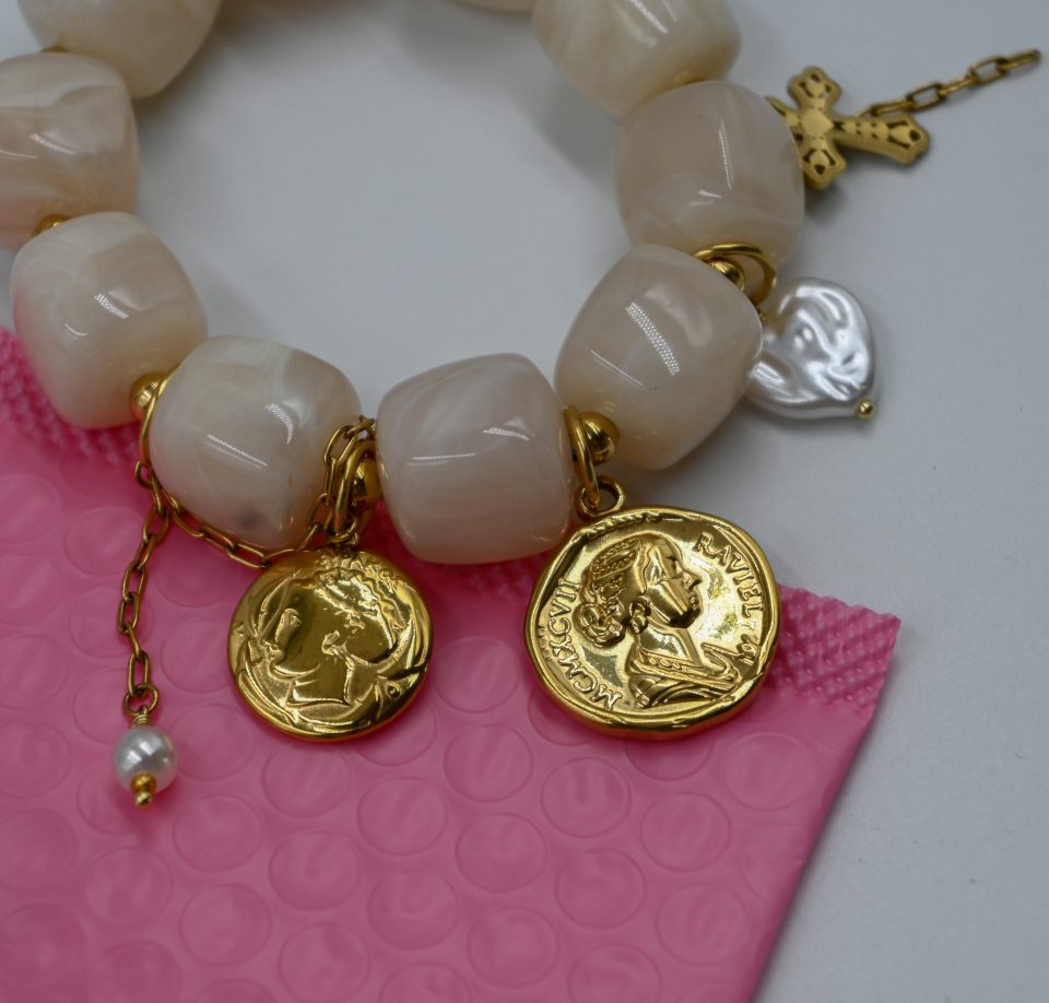 White resin charm bracelet with gold-plated steel details, coins, pearls, chains, and cross charm. A bold and unique summer statement piece.