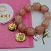 Pink resin charm bracelet with gold-plated steel charms, coins, pearls, chains, and carved cross. A bold and radiant summer statement piece.
