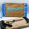 Blue raffia clutch bag with zipper closure, spacious interior, embroidered Jamaica design, and detachable fabric shoulder strap.