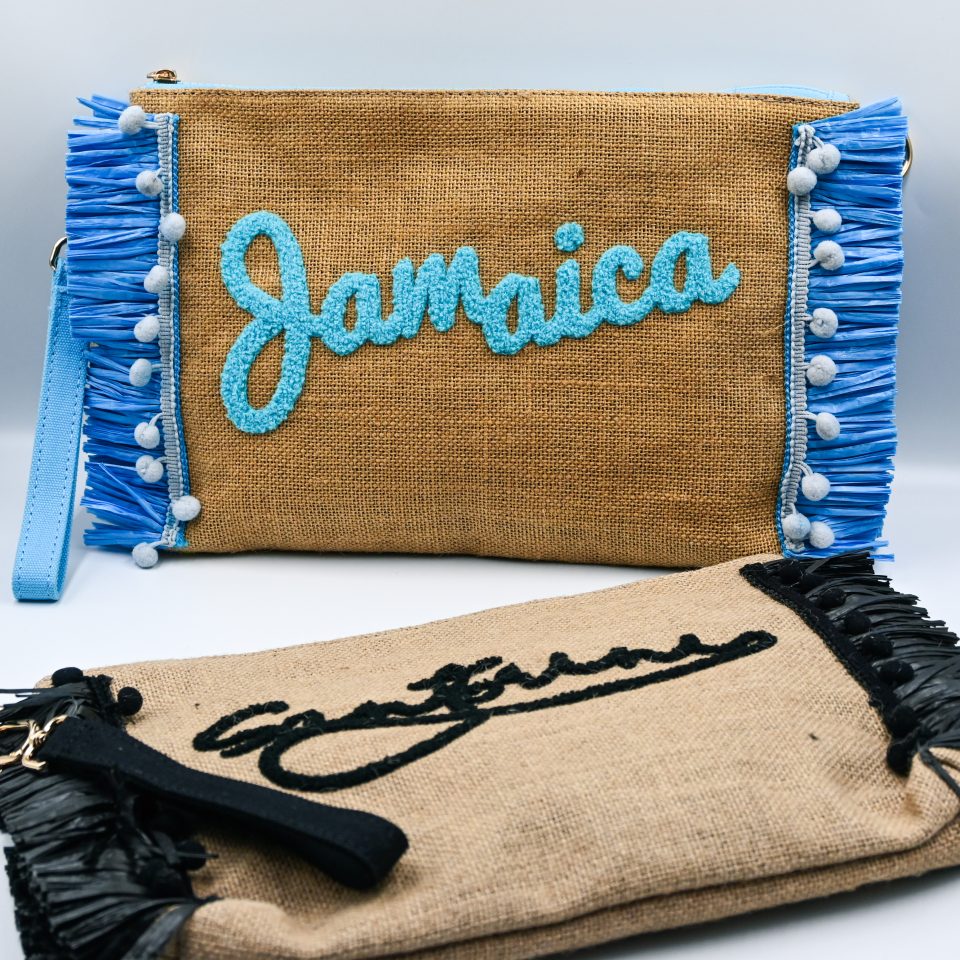 Blue raffia clutch bag with zipper closure, spacious interior, embroidered Jamaica design, and detachable fabric shoulder strap.
